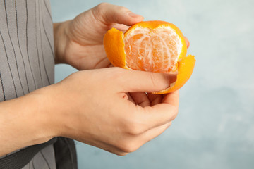 Woman peeling ripe tangerine on light background, closeup