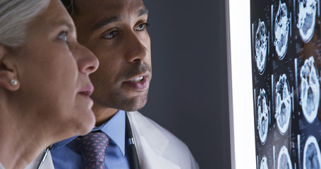 Tight shot of millennial african-american doctor discussing with senior colleague patient ct scans. Close up of two medical physicians consulting over xrays of cranium © Mark Adams