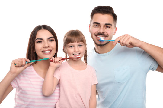 Little girl and her parents brushing teeth together on white background