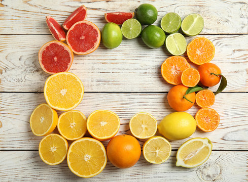 Frame made of different citrus fruits on wooden background, top view. Space for text