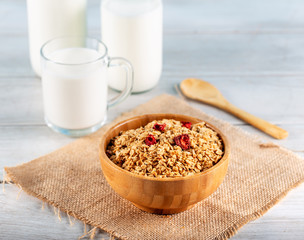Rolled oats or oat flakes in bowl with wooden spoonsand bottle of milk on background.
