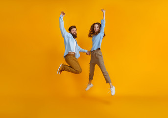 couple of emotional people man and woman jumping on yellow background.
