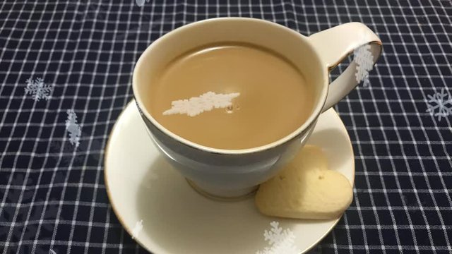Cinemagraph -ed snow falling on the white cup of coffee with heart shaped cookie on a table with a checkered tablecloth. Christmas breakfast. Holiday still life. Top view. loseup