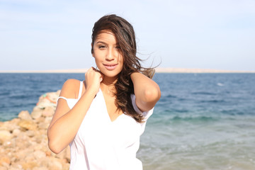 Fototapeta na wymiar Beautiful young girl face portrait, brown hair and nice smile, wearing white tunic, fashion model look with a sea landscape. Female woman photo session for fashion beauty competition, middle eastern
