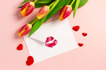 Valentine's day background. Love letter concept. White envelope with red lipstick kiss, red hearts and bouquet of tulips on pink pastel.