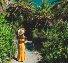 Young girl in yellow dress and hat have rest in palm forest of Preveli, Crete, Greece