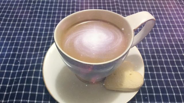 Cinemagraph - Galaxy in the cup of coffee. Steaming white cup of coffee with rotating galaxy in it on a table with a checkered tablecloth