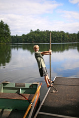 Naklejka premium Child Playing on Dock by Fishing Row Boat on Small Lake in Northern Woods
