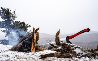 Bonfire in the winter forest on the snow from dry wood, harvested by a small red ax.
