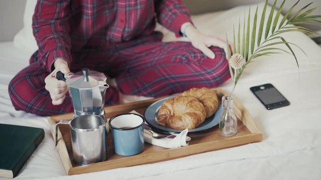 Female in checkered pajamas having breakfast in bed Preparing or pouring coffee and making picture or smartphone or mobile phone photo of food tray or morning meal and share in bedroom after wake up