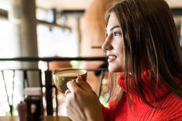 Beautiful smiling woman drinking coffee at cafe. Portrait of mature woman in a cafeteria drinking hot cappuccino and looking at camera. Pretty woman with cup of coffee.