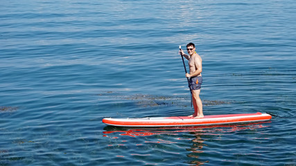 Friendly young man active with paddel-board on Lake Constance
