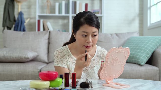 young female famous blogger using brush and pink lipstick makeup looking at mirror in living room marble table. beautiful woman showing cosmetic and lips at live shop online video streaming. 