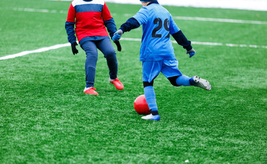 Obraz premium Two young Footballers in red and blue sportswear running,dribble and competing for ball. Junior football match competition. Winter activities, soccer game, training concept