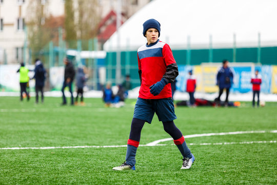 Boy in red and blue sportswear plays soccer on green grass field. Youth football game. Children sport competition, kids plays outdoor, winter activities, training