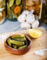 Bowl of pickled cucumbers and jars of pickled vegetables on wooden background