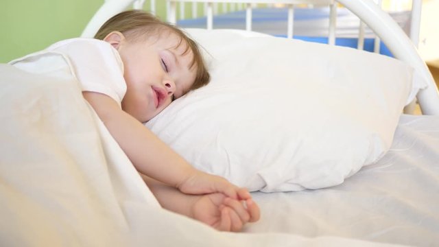 Little baby sleeping in hospital ward on white bedclothes. Treatment of children in hospital setting. Sick kid improves his health in hospital.