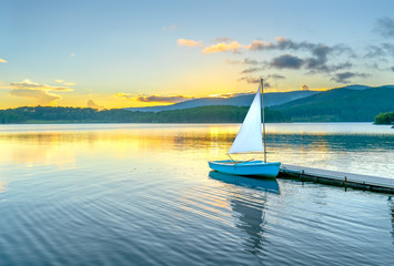 Lonely sailboat in the beautiful sunset with sun stars shines from sky and the surface of the lake...