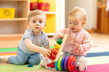funny babies boy and girl playing on floor in game room in nursery