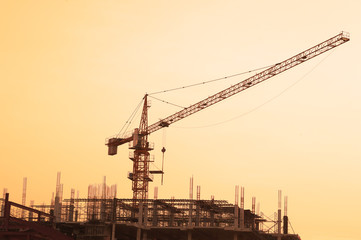 Fototapeta premium Silhouette building crane and buildings under construction against evening sky.