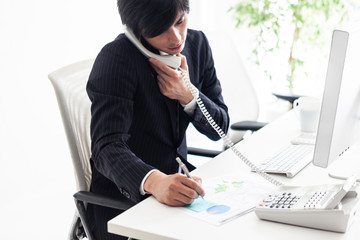 メモを取りながら電話の受け答えをする男性会社員