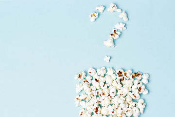 Question mark laid out of popcorn on a blue background close-up, top view, texture