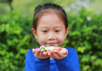 Asian child girl holding some thai sugar and fruit toffee with colorful paper wrapped in her hands. Focus at candy in her hands.