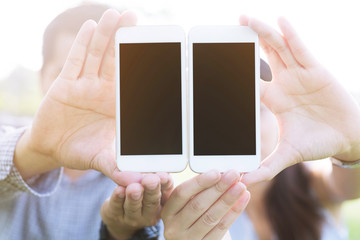 close up of two young male and female  hand holding display white mobile smart phone with blank of empty screen at the outdoors public park.