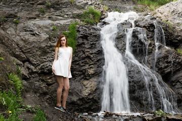 Girl in white summer dress on the background of a waterfall. Girl cold, cold weather and a girl in...
