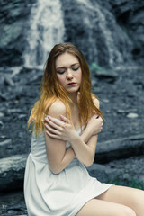 Girl in white summer dress on the background of a waterfall. Girl cold, cold weather and a girl in...