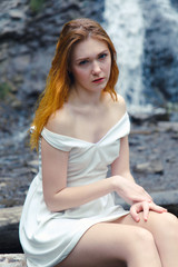 Girl in white summer dress on the background of a waterfall. Girl cold, cold weather and a girl in...
