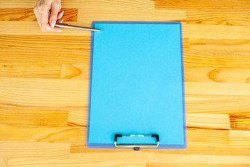 Office Hand Holding a Folder with a Blue Color Paper and Pen on the Colored Background of the Wooden Table. Copyspace. Place for Text