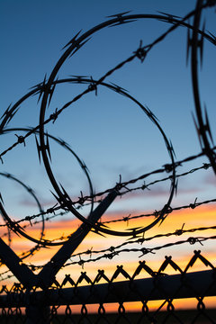 Dramatic sunset with chain link fence and razor wire silhouette.