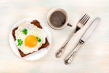An overhead photo of an egg cooked sunny side up on a toast with coffee and copy space