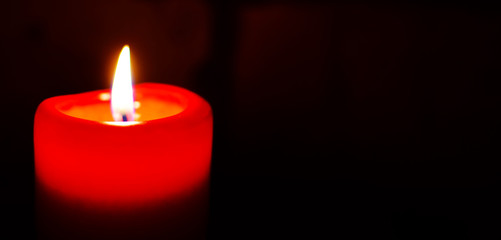 One red candle burning in darkness with empty free space for text. Advent or memorial prayer candle flame.