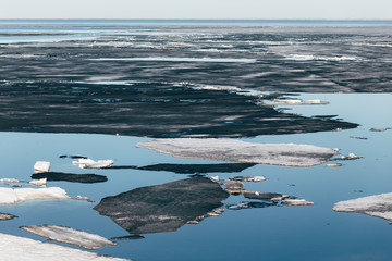 Huge black ice floes on blue water surface. Spring background