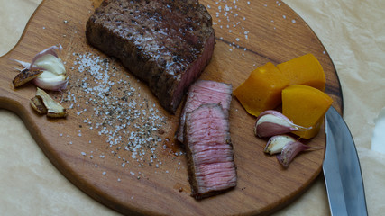 Extreme Close Up view of a Hand Seasoning Cooked piece of Meat in a Bright Light. Chef Accompanying Steak with Garlic, Rosemary, Pepper, Salt. Delicious, Modern Cuisine, Exclusive Recipe. 