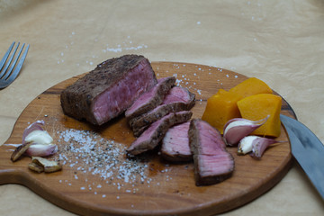 Extreme Close Up view of a Hand Seasoning Cooked piece of Meat in a Bright Light. Chef Accompanying Steak with Garlic, Rosemary, Pepper, Salt. Delicious, Modern Cuisine, Exclusive Recipe. 