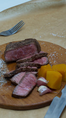 Extreme Close Up view of a Hand Seasoning Cooked piece of Meat in a Bright Light. Chef Accompanying Steak with Garlic, Rosemary, Pepper, Salt. Delicious, Modern Cuisine, Exclusive Recipe. 