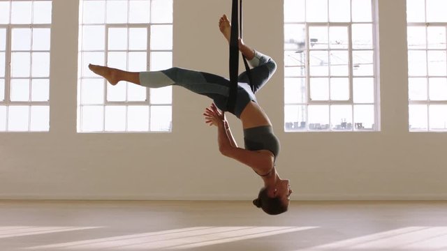 aerial yoga woman practicing bound one-legged king pigeon pose hanging upside down using hammock enjoying healthy fitness lifestyle exercising in studio training meditation at sunrise