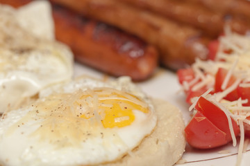 Fried rustic sausage links with sunny side up eggs with tomato and shreded aged cheese salad