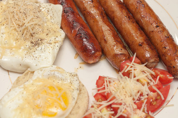 Fried rustic sausage links with sunny side up eggs with tomato and shreded aged cheese salad