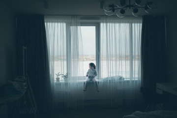 Fototapeta premium Cute little girl sitting on windowsill