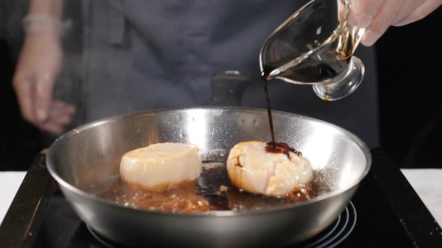 Seafood in restaurant. Vegetarian concept. Professional chef in gloves pouring sauce on scallops in frying pan. Slow motion. hd