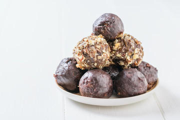 Hand-made balls of dried fruits, nuts and chocolate in a bowl on a white wooden table.