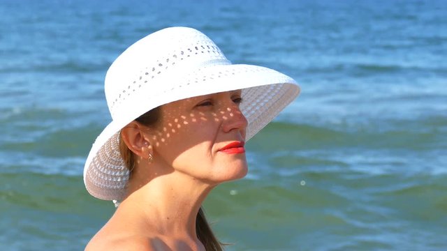    4K. Face of pretty woman in white hat, standing near ocean waves