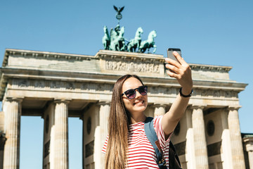 Young beautiful positive girl makes selfie against the background of the Brandenburg Gate in Berlin...