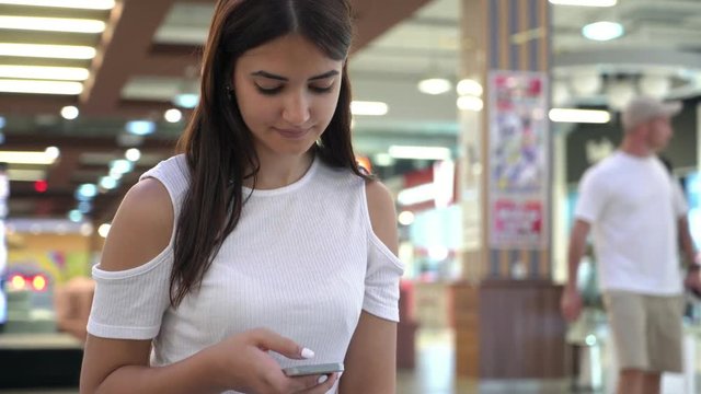Smiling brunette woman sitting and browsing the internet on her phone in a mall   