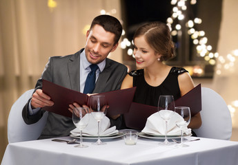 dating, luxury and people concept - happy couple with menus at restaurant over festive lights on background