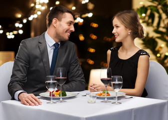 people and leisure concept - smiling couple with food and non-alcoholic red wine talking at restaurant over festive lights on background